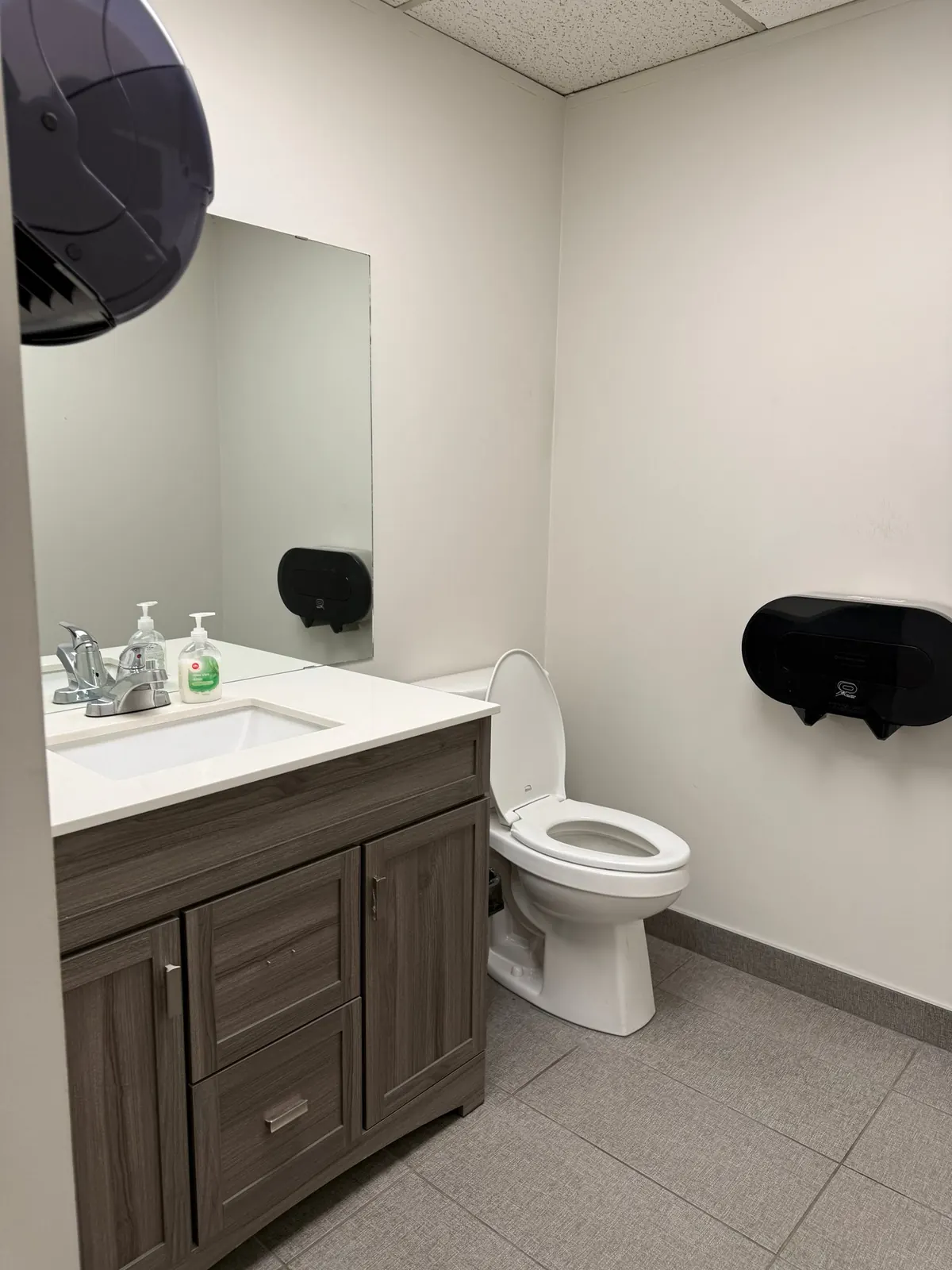 Clean office washroom with a wood vanity, white sink, mirror and spotless tile floor after a Celestial office clean